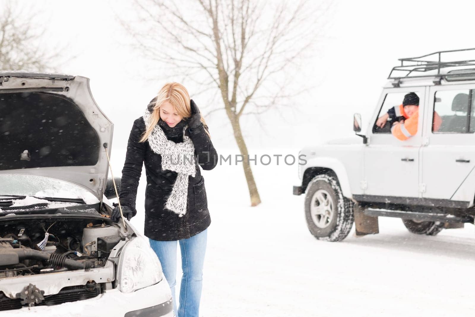 Woman looking under broken car hood snow trouble man assistance