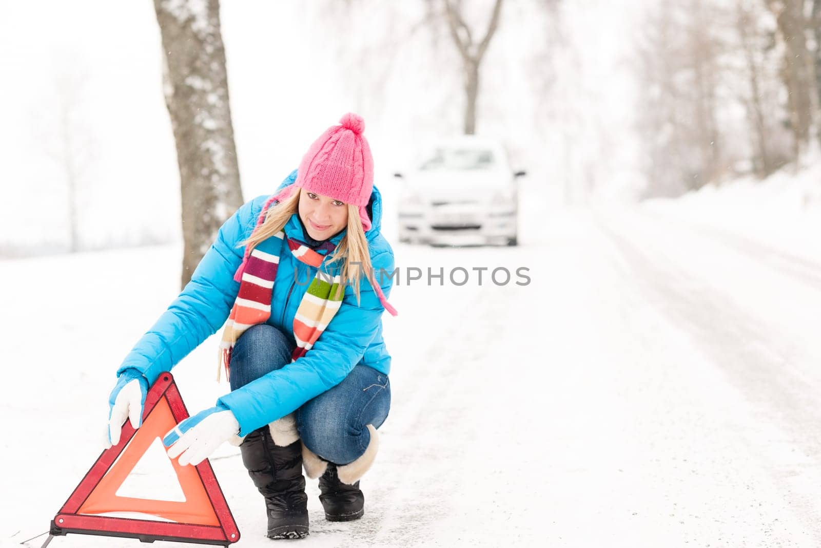 Woman putting reflector triangle car breakdown winter snow sign
