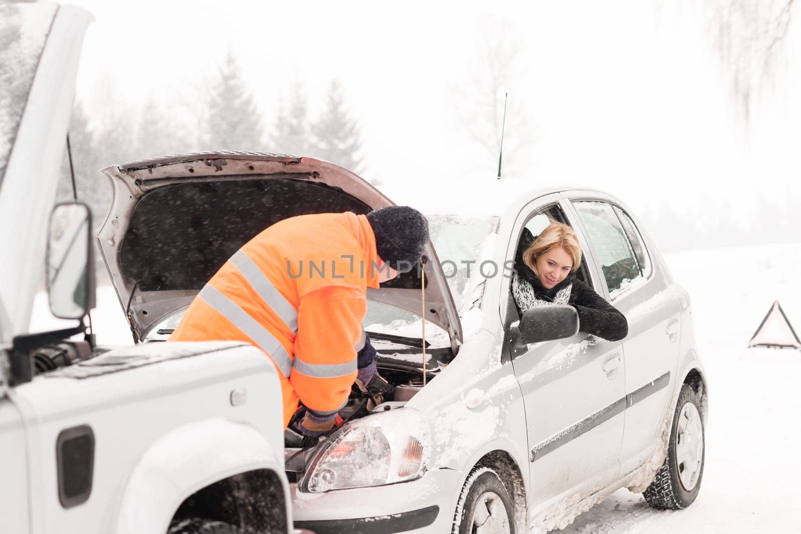 Man repairing woman's car snow assistance winter broken tools mechanic