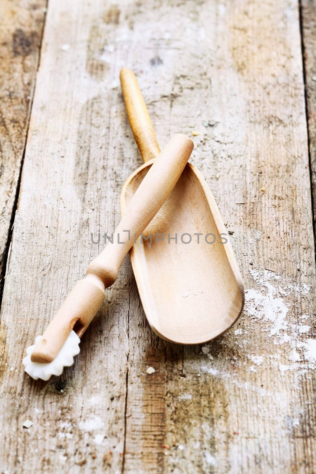 Wooden pizza cutter and flour shovel with remnants of flour in a rustic kitchen on an old grainy textured wood surface