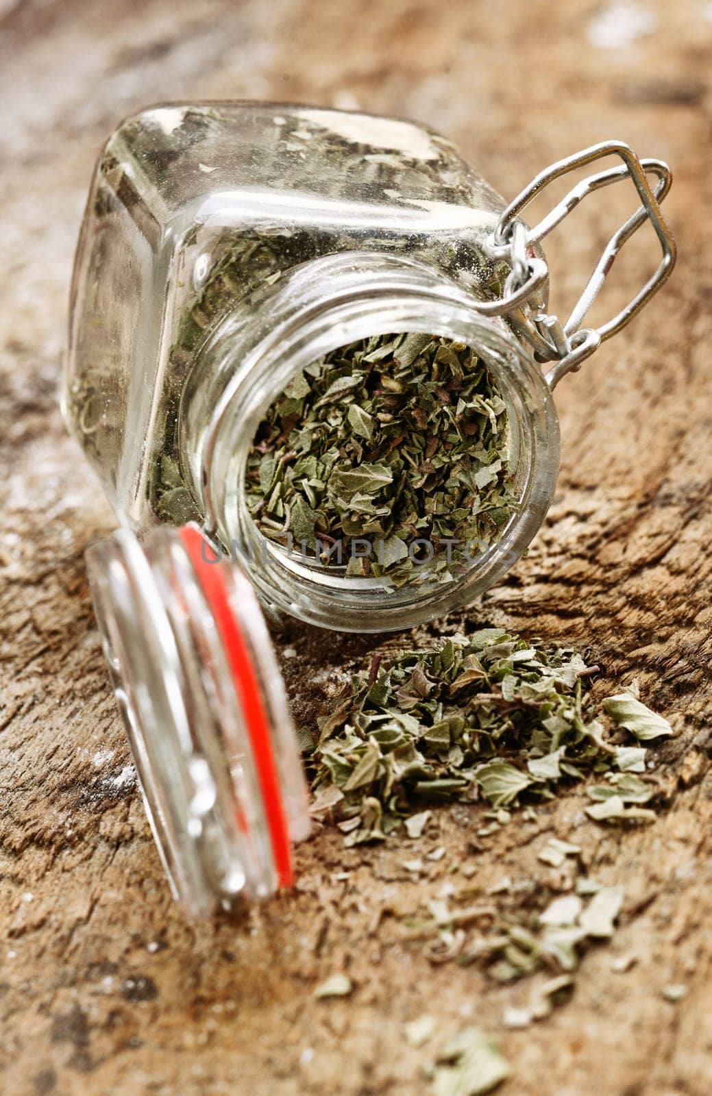 Dried cooking herbs in an opened glass bottle lying on its side spilling out onto an old rustic wooden tabletop