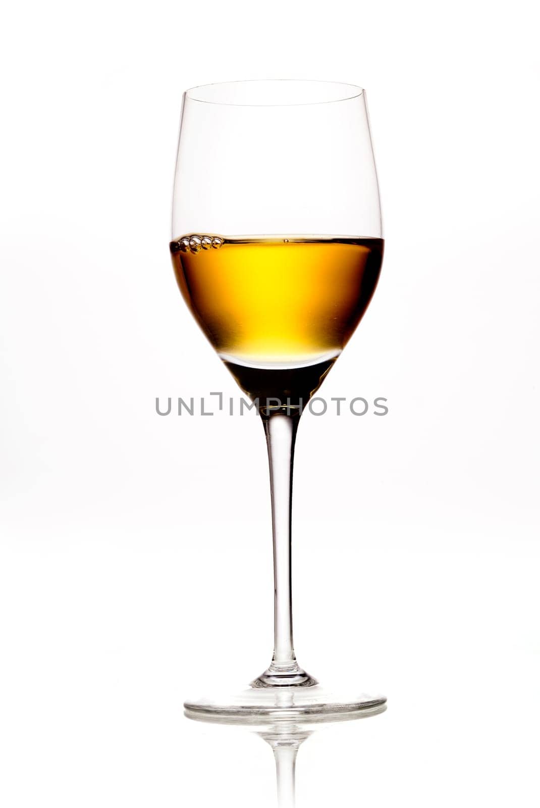 Elegant wineglass full of amber coloured wine or sherry on a white background with reflecton