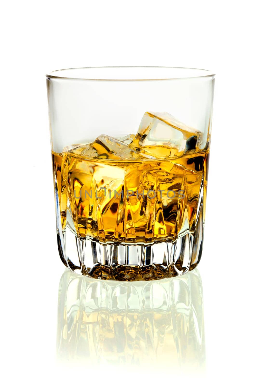 Closeup of a tumbler of glowing golden brandy and ice on a white background with relection