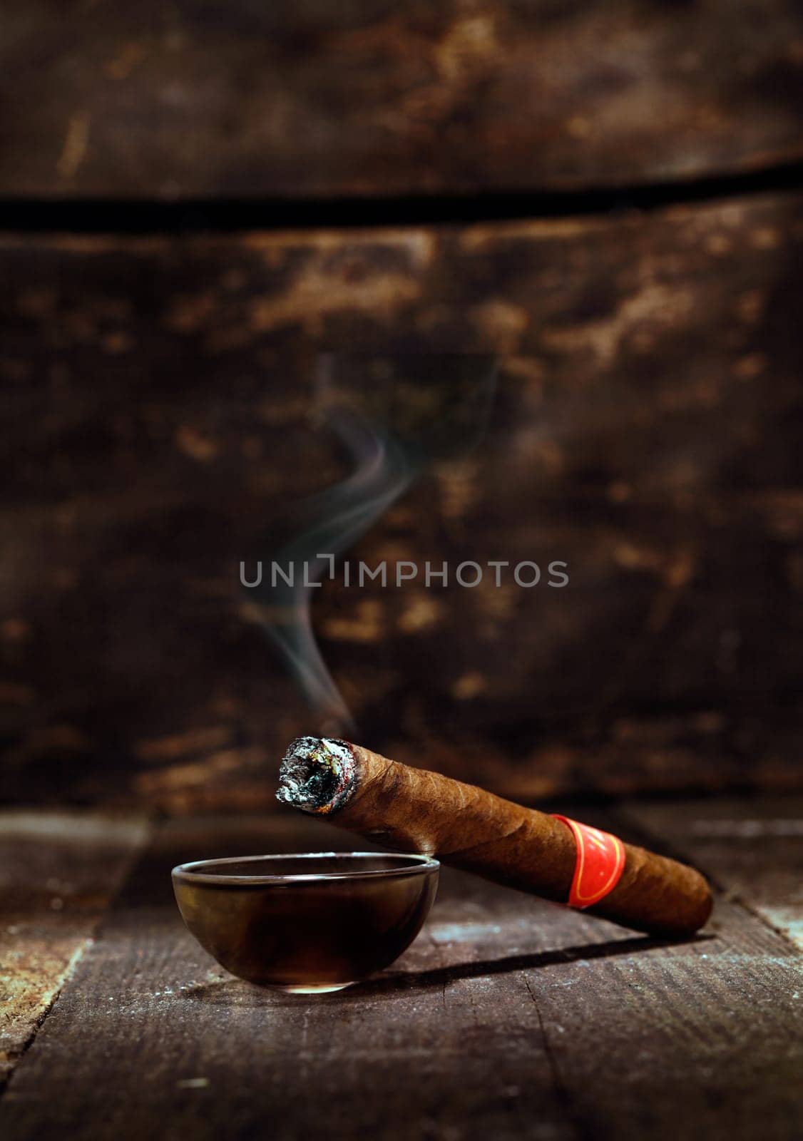 Burning handmade luxury Cuban cigar resting on an ashtray on an old wooden countertop in a nightclub or bar with copyspace