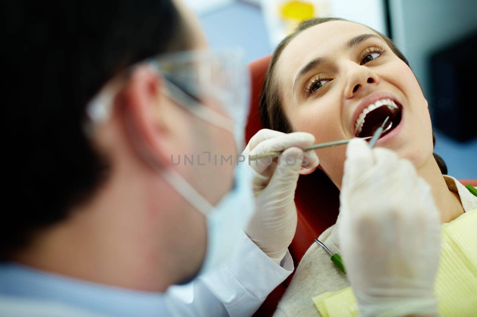 Smiling woman sitting in dentists chair while doctor examining her teeth