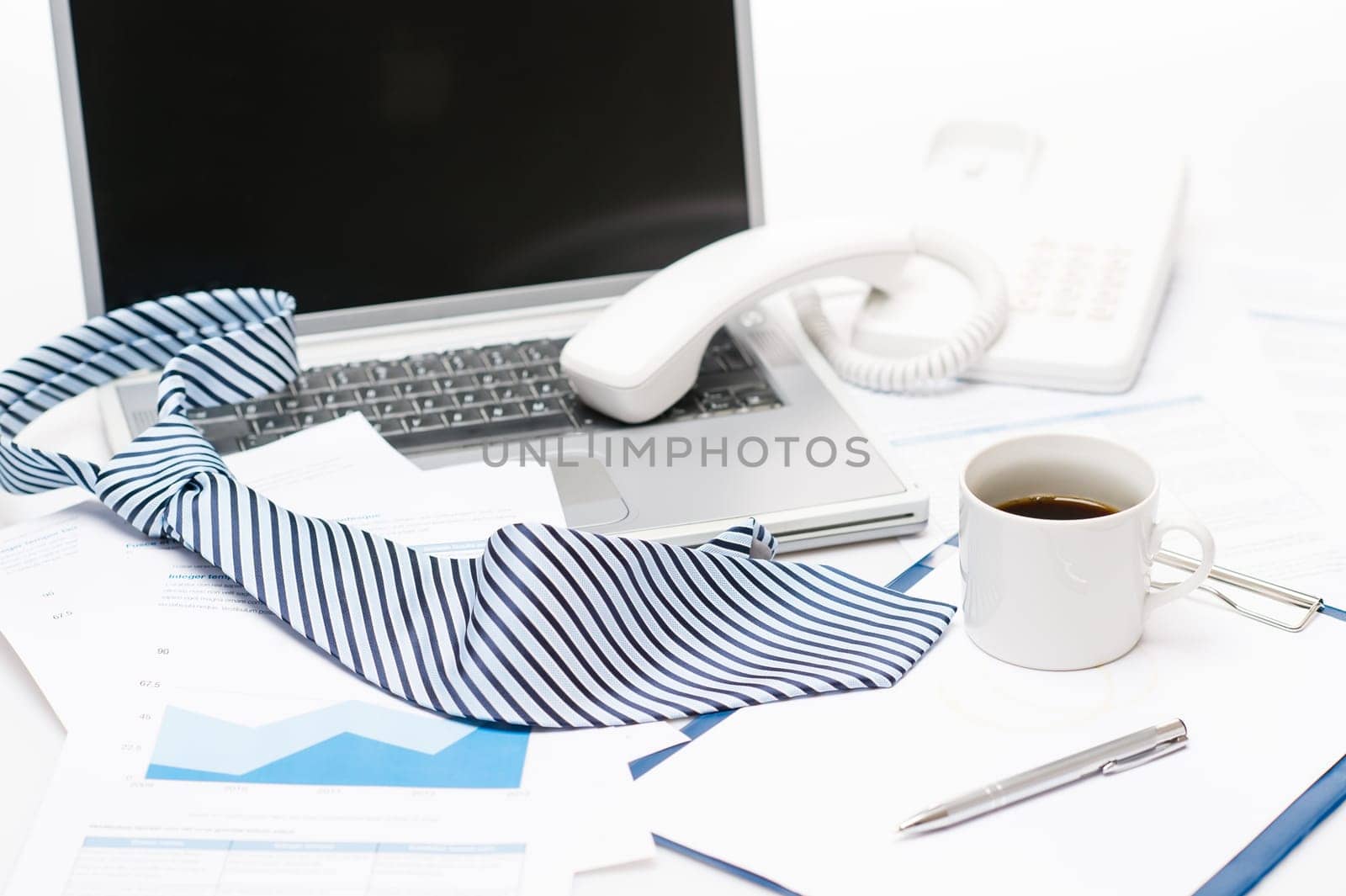 Man's tie laying on business office desk over laptop charts
