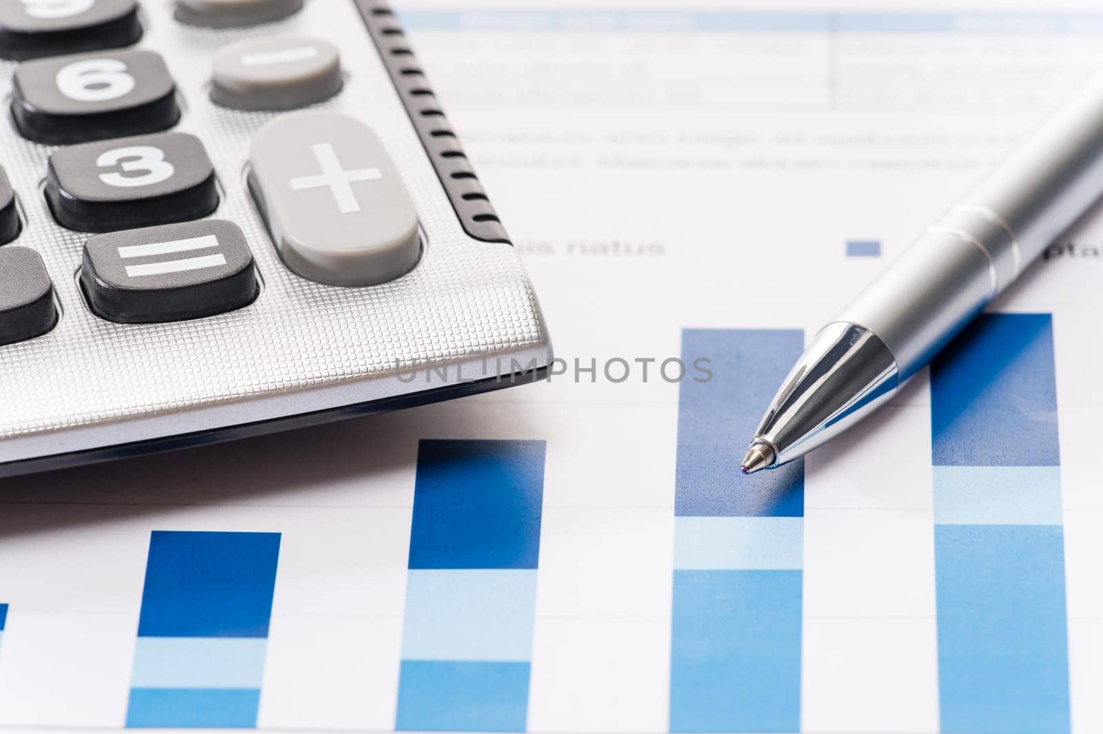 Business silver pen and calculator over office charts close-up