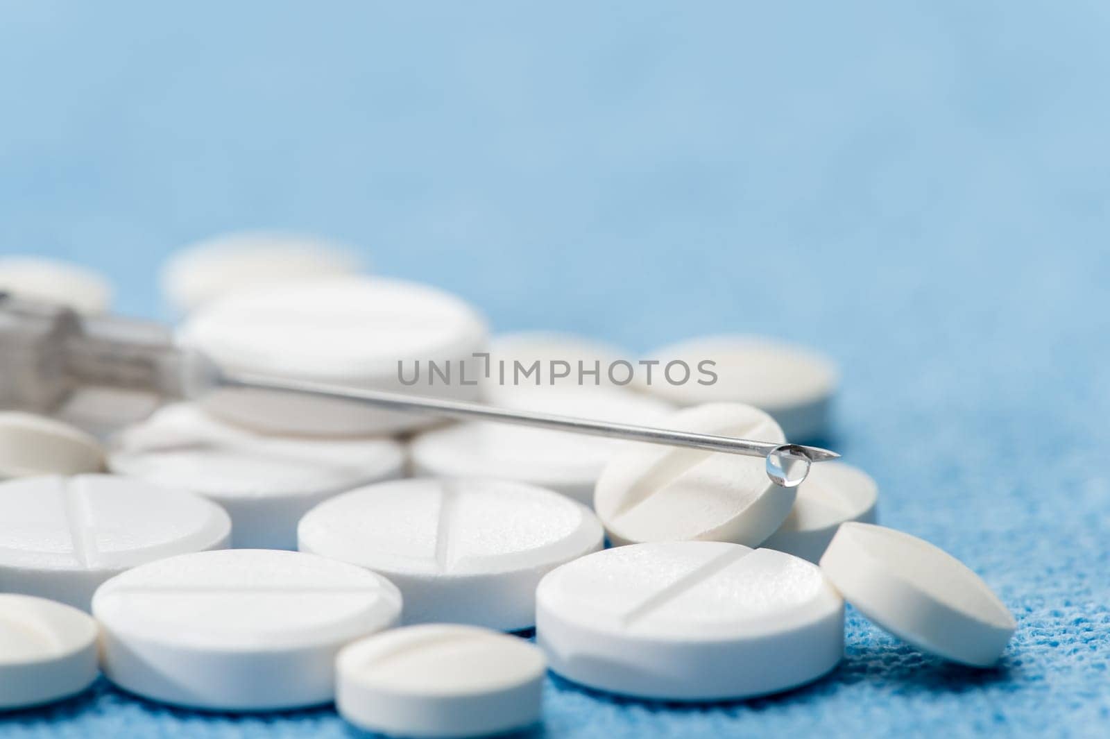 Hypodermic needle with drip medication spilled capsules on blue background