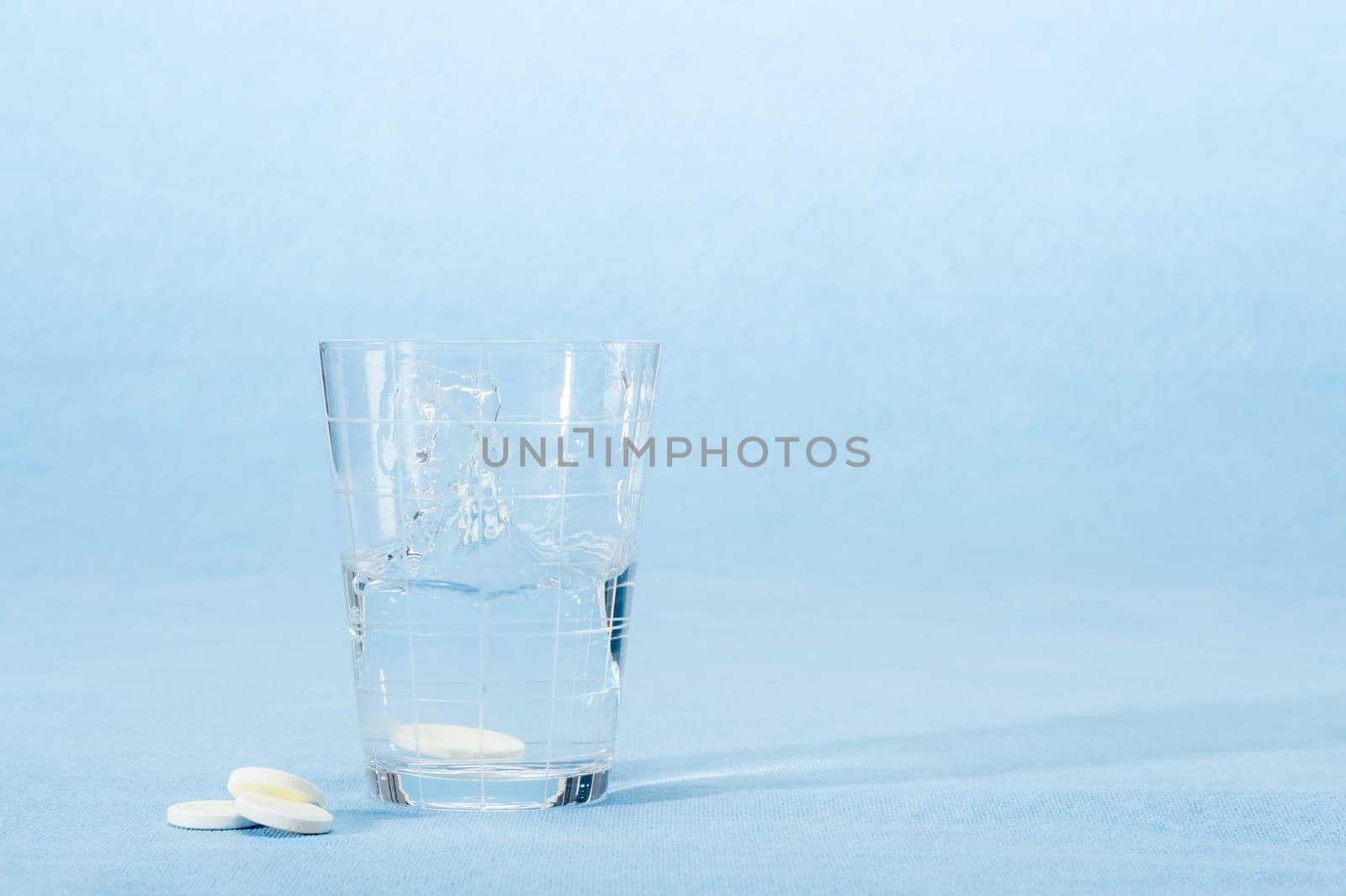 Fizzy vitamin capsule throw in water glass on blue background