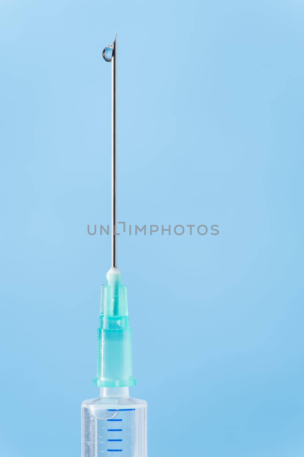 Medical syringe drop falling from needle on blue background