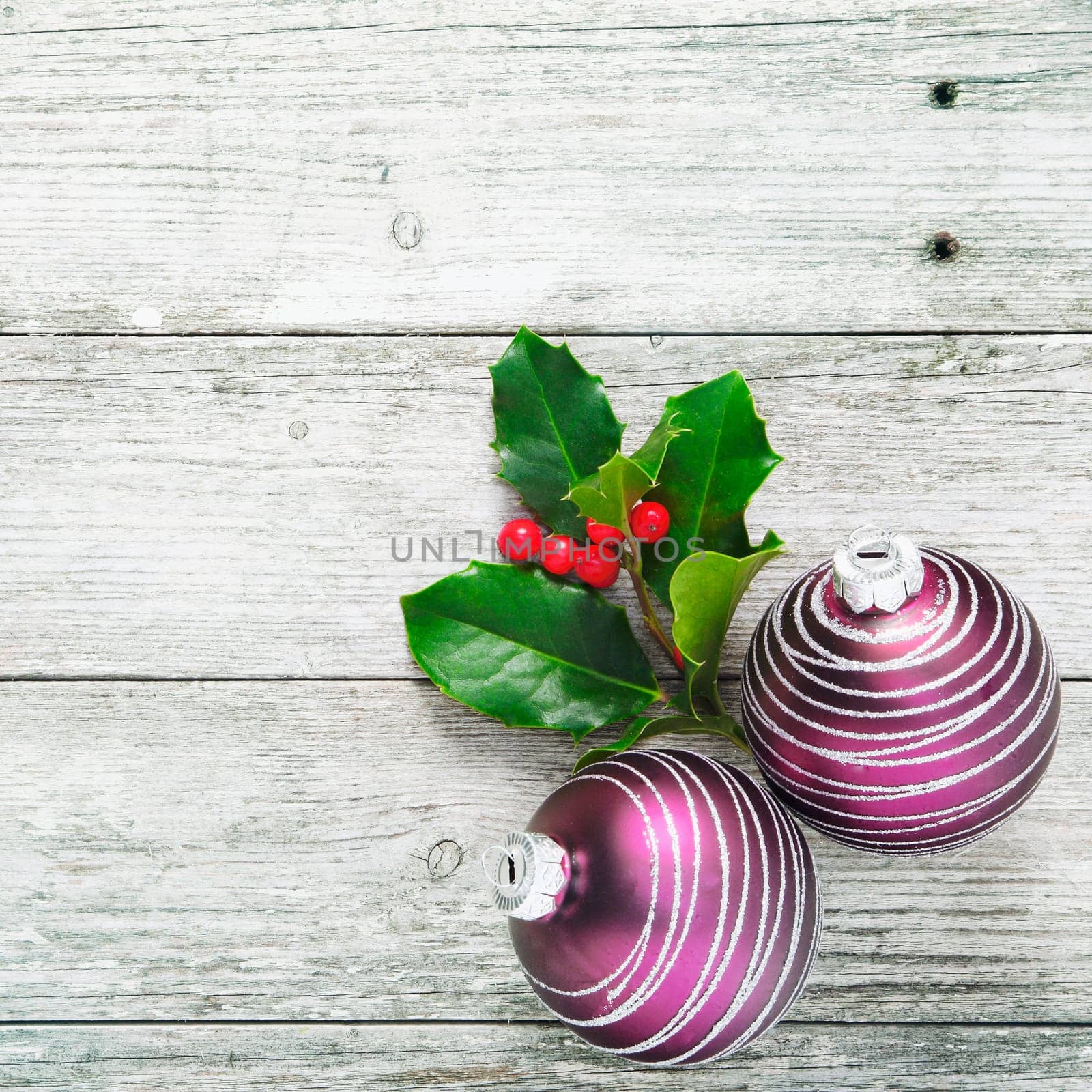 Rustic Christmas background with decorative holly and baubles on woodgrain texture white painted boards in square format with copyspace