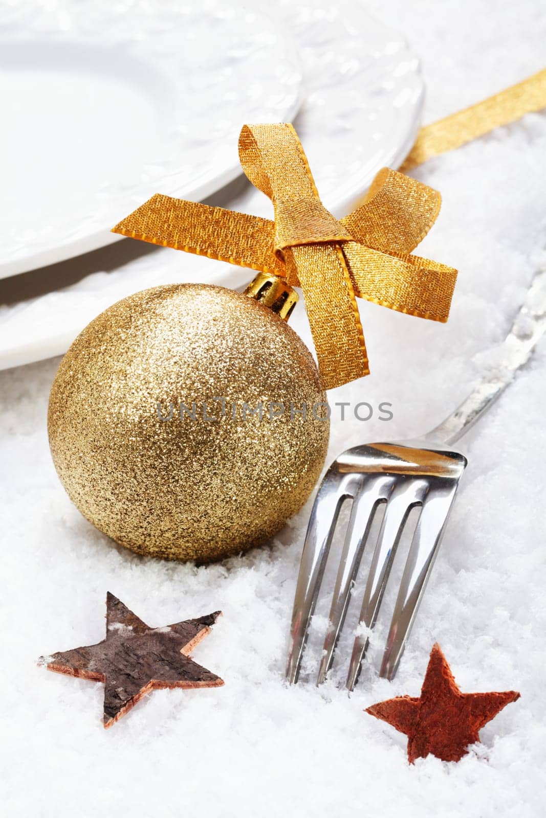 Christmas winter place setting on snow with silver cutlery decorated with a golden bauble and stars