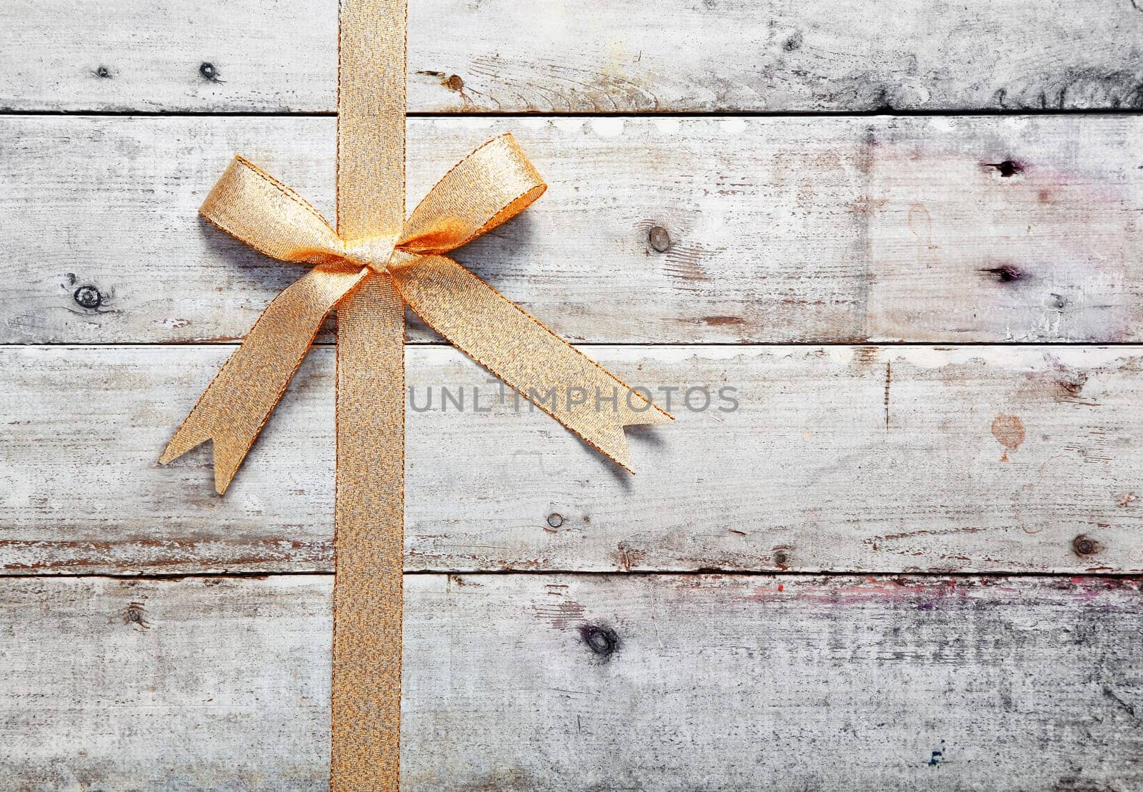 Decorative golden bow and ribbon on old rustic wooden boards with woodgrain copyspace for your Christmas, birthday or anniversary message