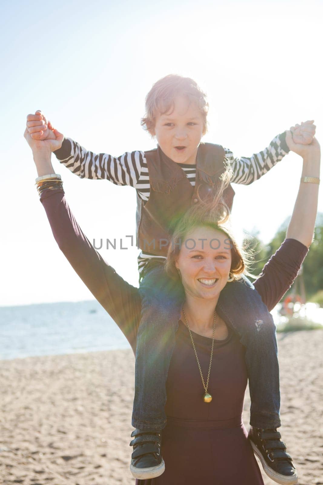 Mother carrying son on shoulders and having fun together at the beach.