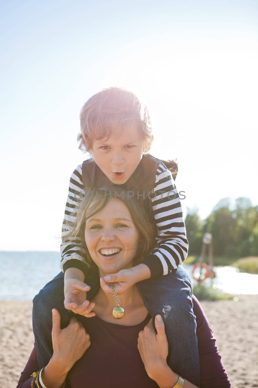 Mother carrying son on shoulders and having fun together at the beach.