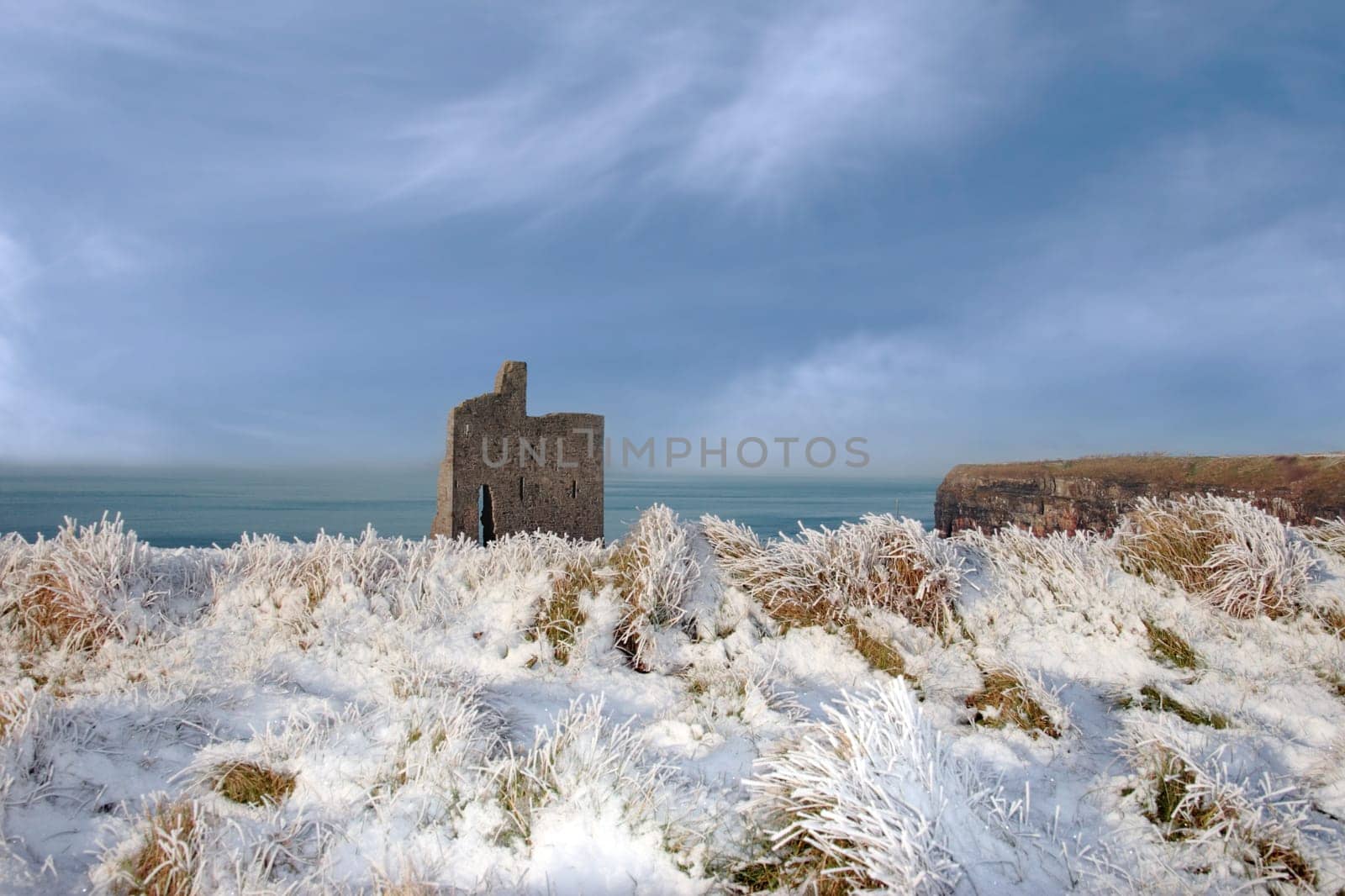 a seasonal snow covered view of atlantic ocean and ballybunion castle and cliffs on a frosty snow covered winters day