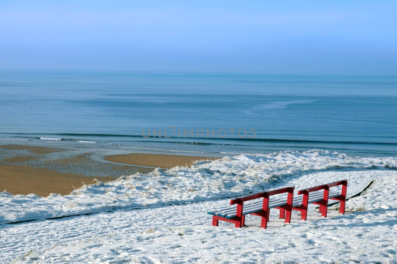 a seasonal snow covered view of atlantic ocean and ballybunion beach with red benches on a frosty snow covered winters day