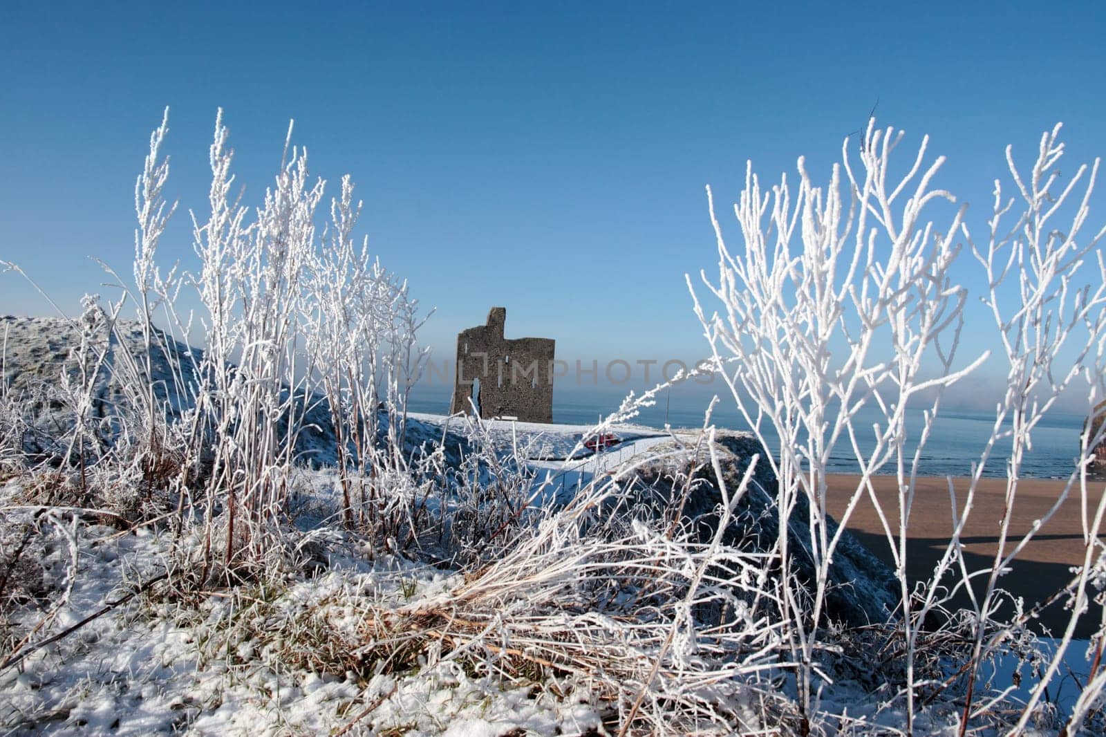 a seasonal snow covered view of atlantic ocean and ballybunion castle beach and cliffs on a frosty snow covered winters day