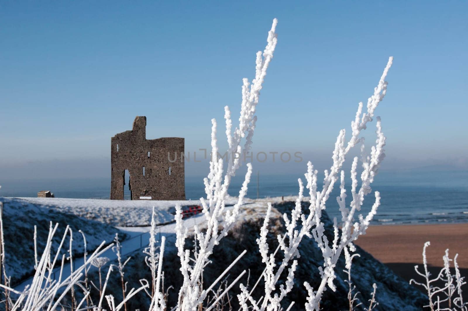 a seasonal snow covered view of atlantic ocean and ballybunion castle beach and cliffs on a frosty snow covered winters day