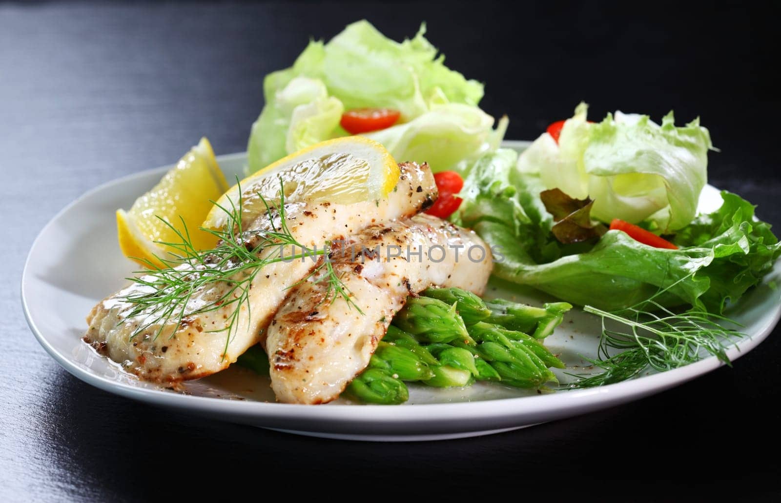 Delicious fried fish on green asparagus with salad