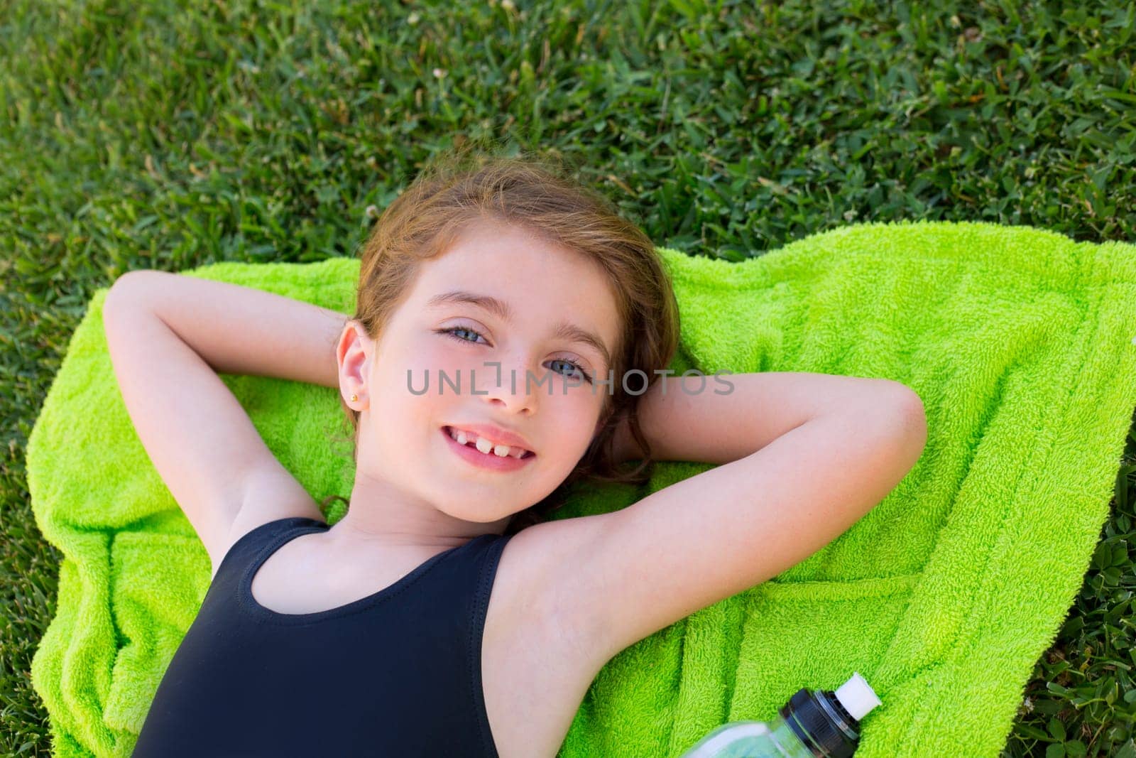 children girl relaxed lying on towel over green grass with water bottle in swimsuit