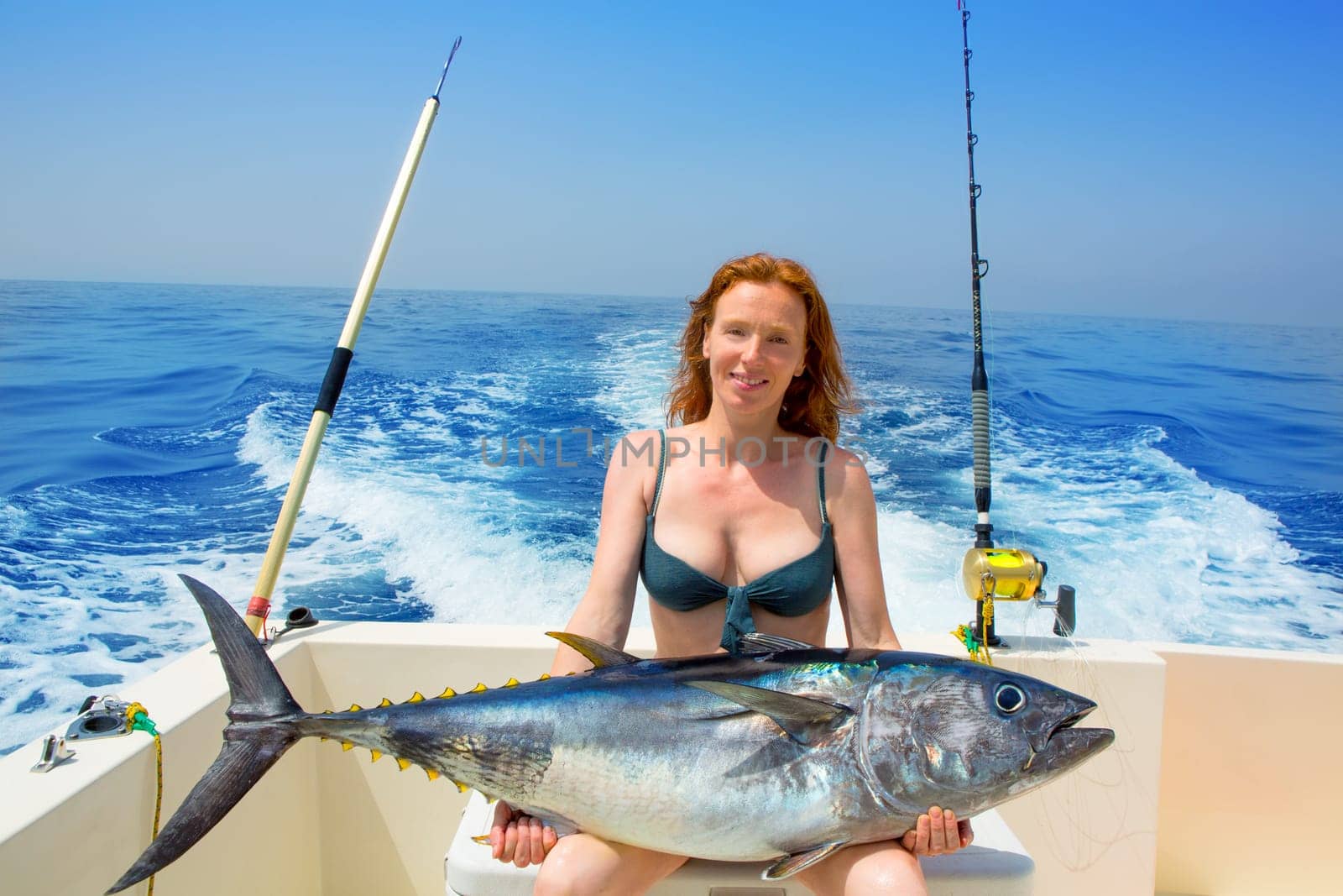 beautiful bikini fisher woman holding big bluefin tuna catch on boat deck