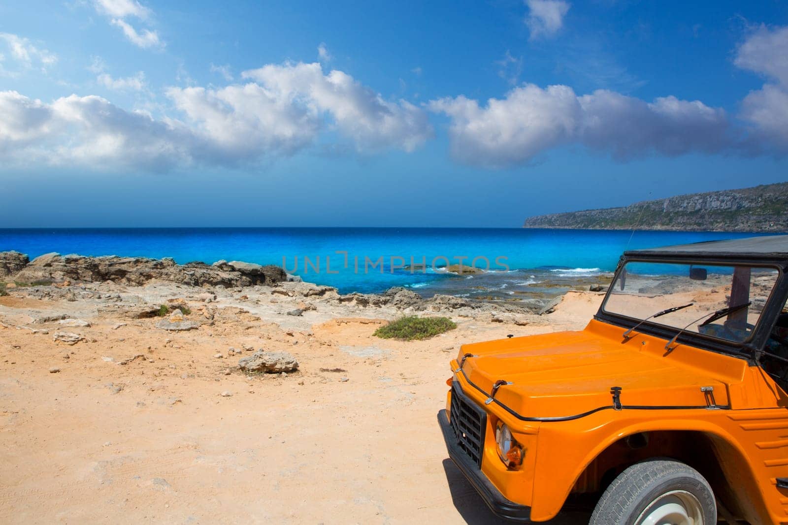 aqua formentera sea Es Calo with vintage retro orange car in Balearics