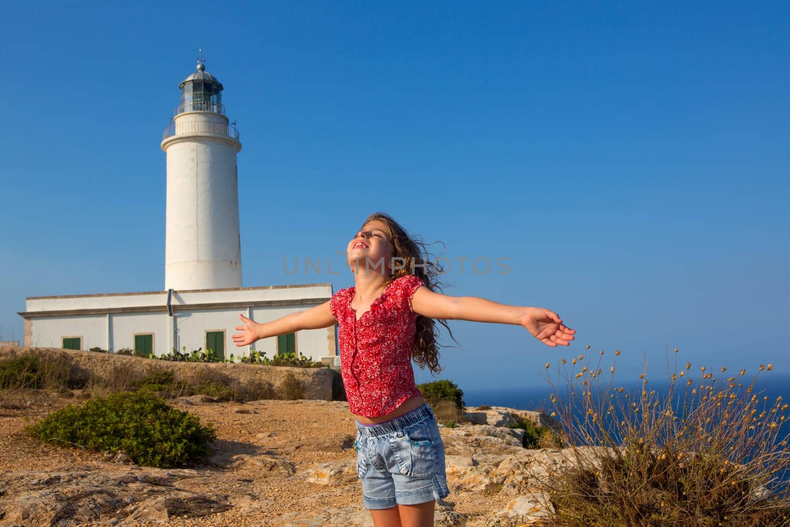 blue day with kid girl open hands to the wind in la Mola lighthouse of Formentera
