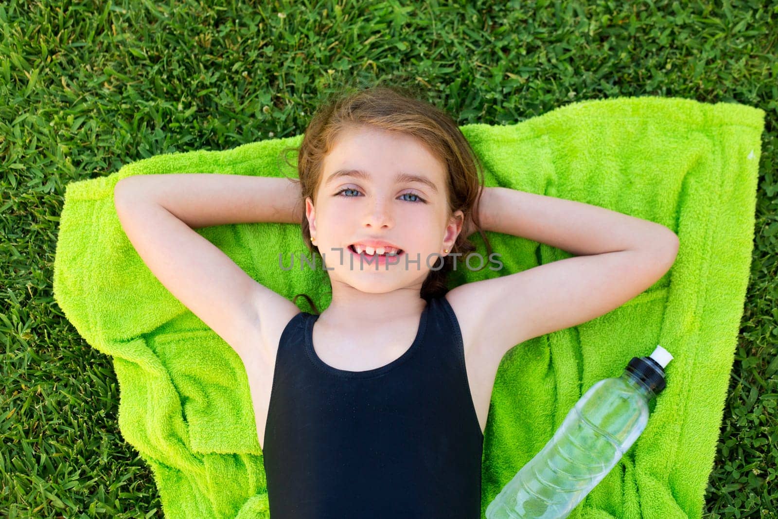 children girl relaxed lying on towel over green grass with water bottle in swimsuit