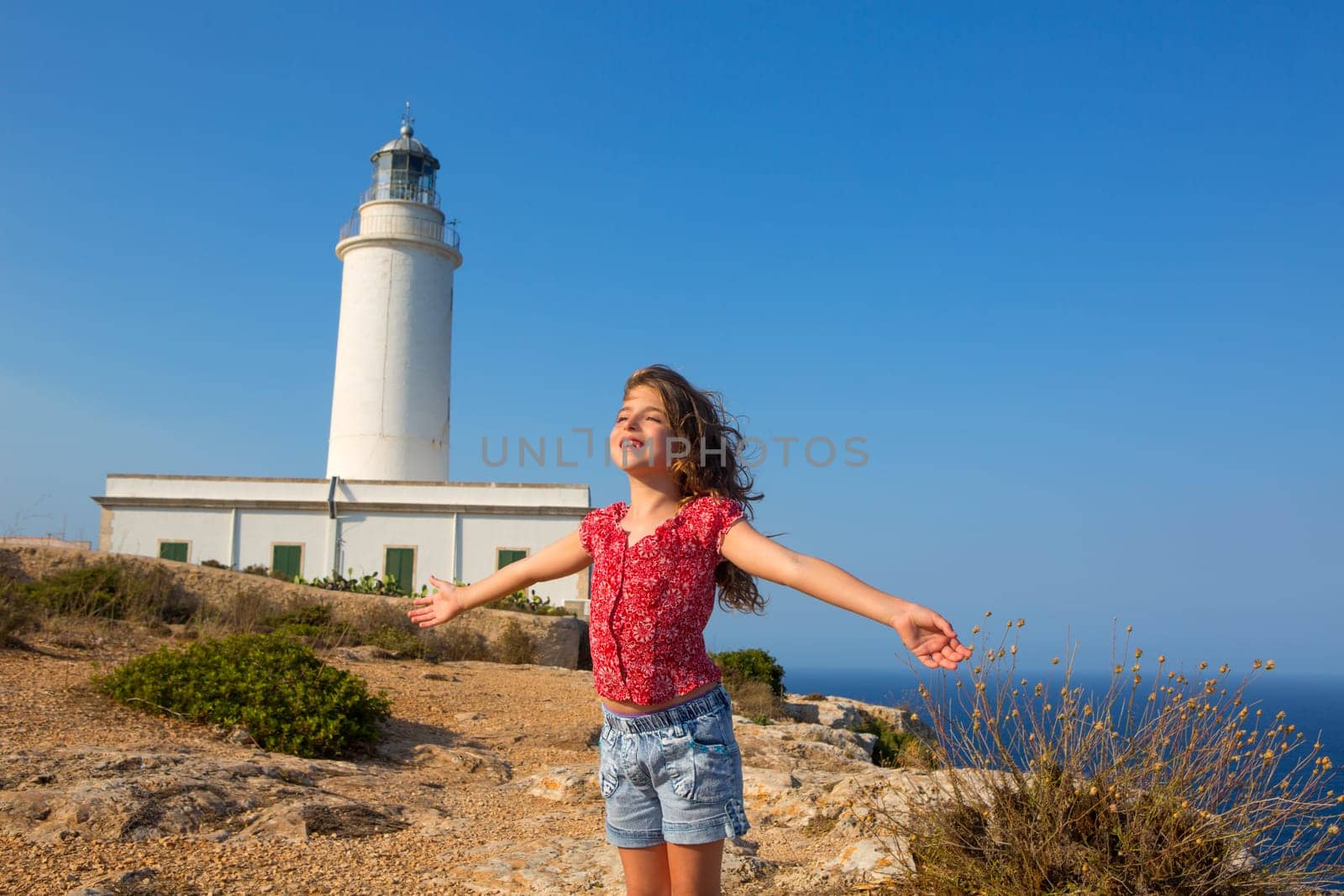 blue day with kid girl open hands to the wind in la Mola lighthouse of Formentera