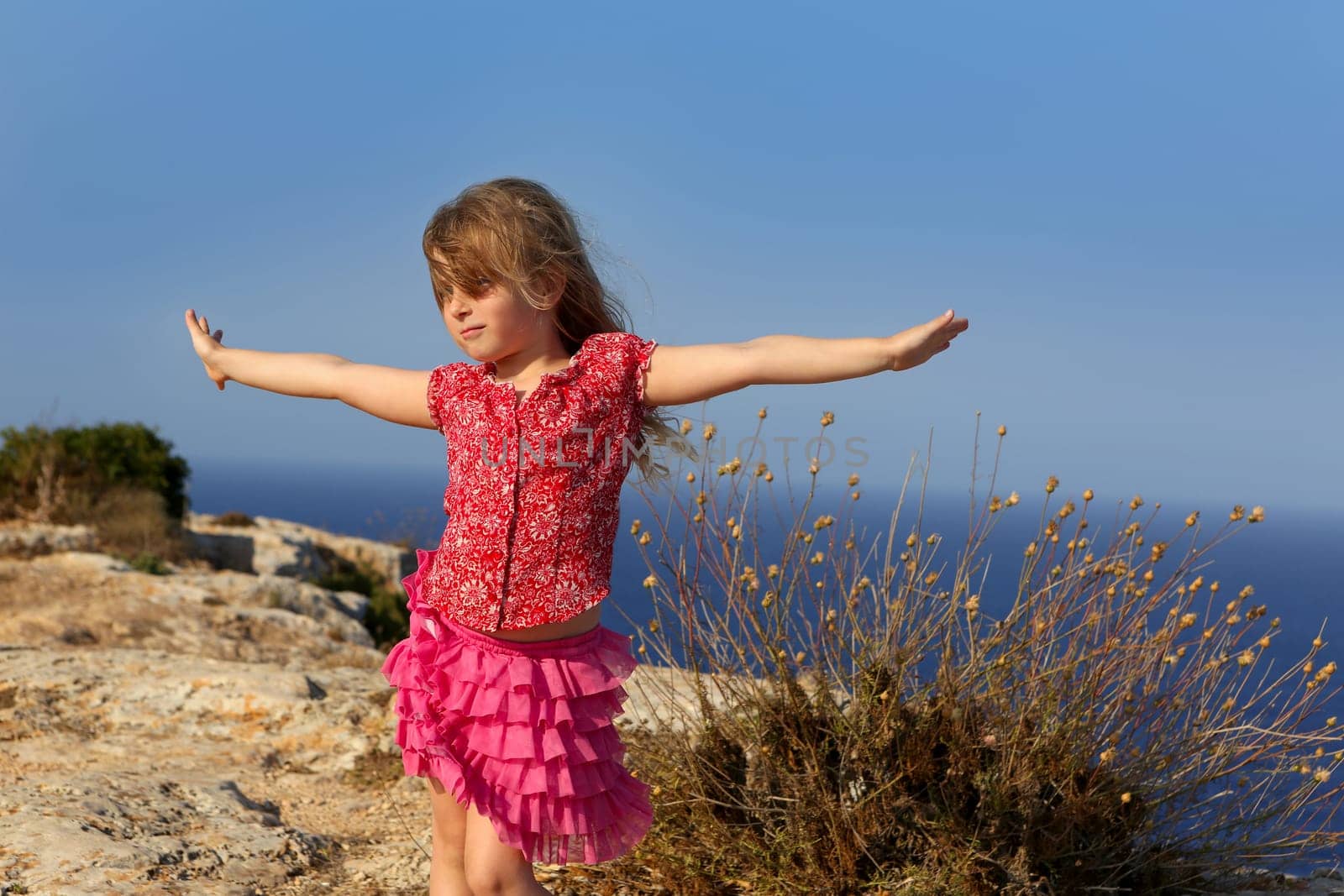 blue day with kid girl open hands to the wind and Mediterranean sea