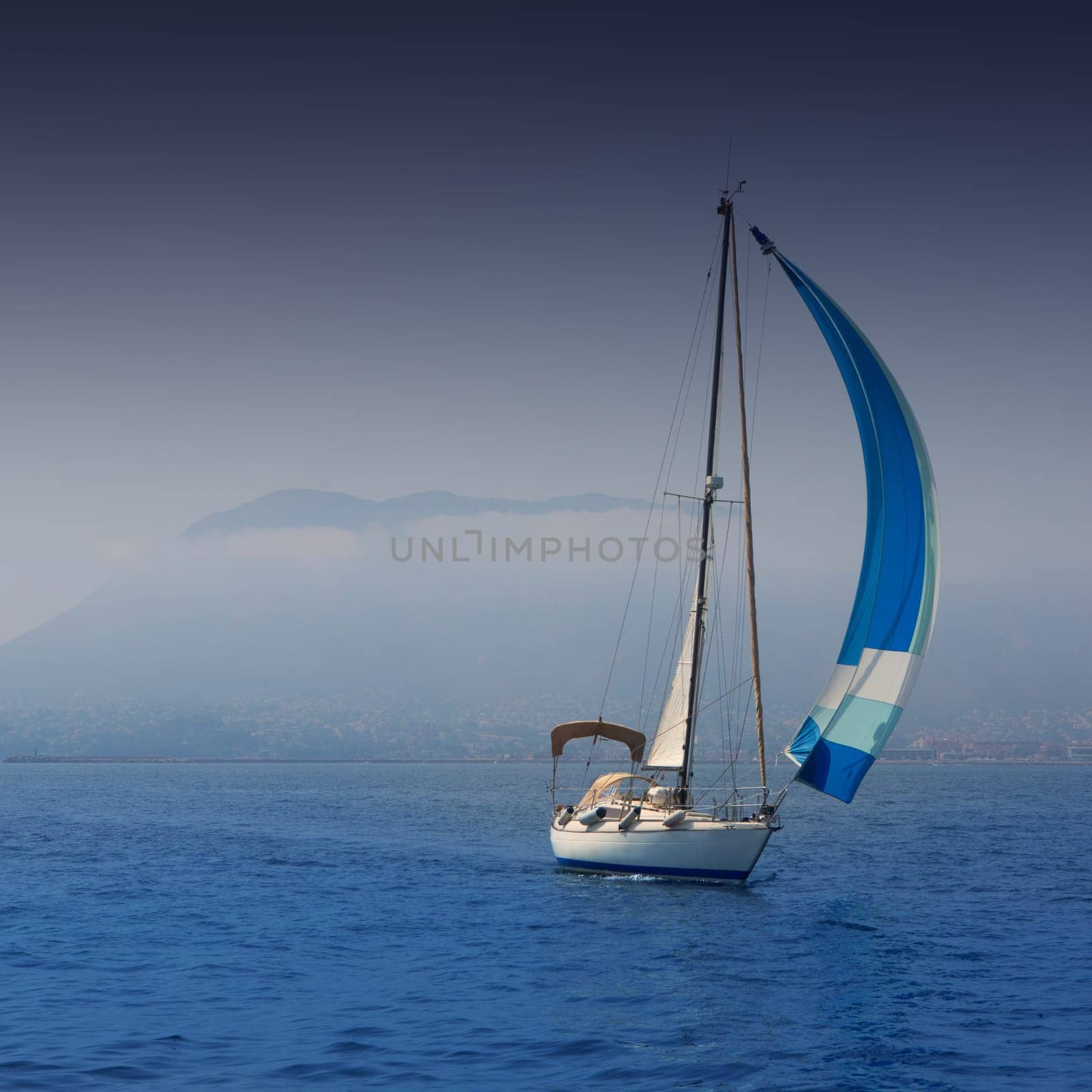 Blue sea with sailboat sailing in a foggy coast in mediterranean sea