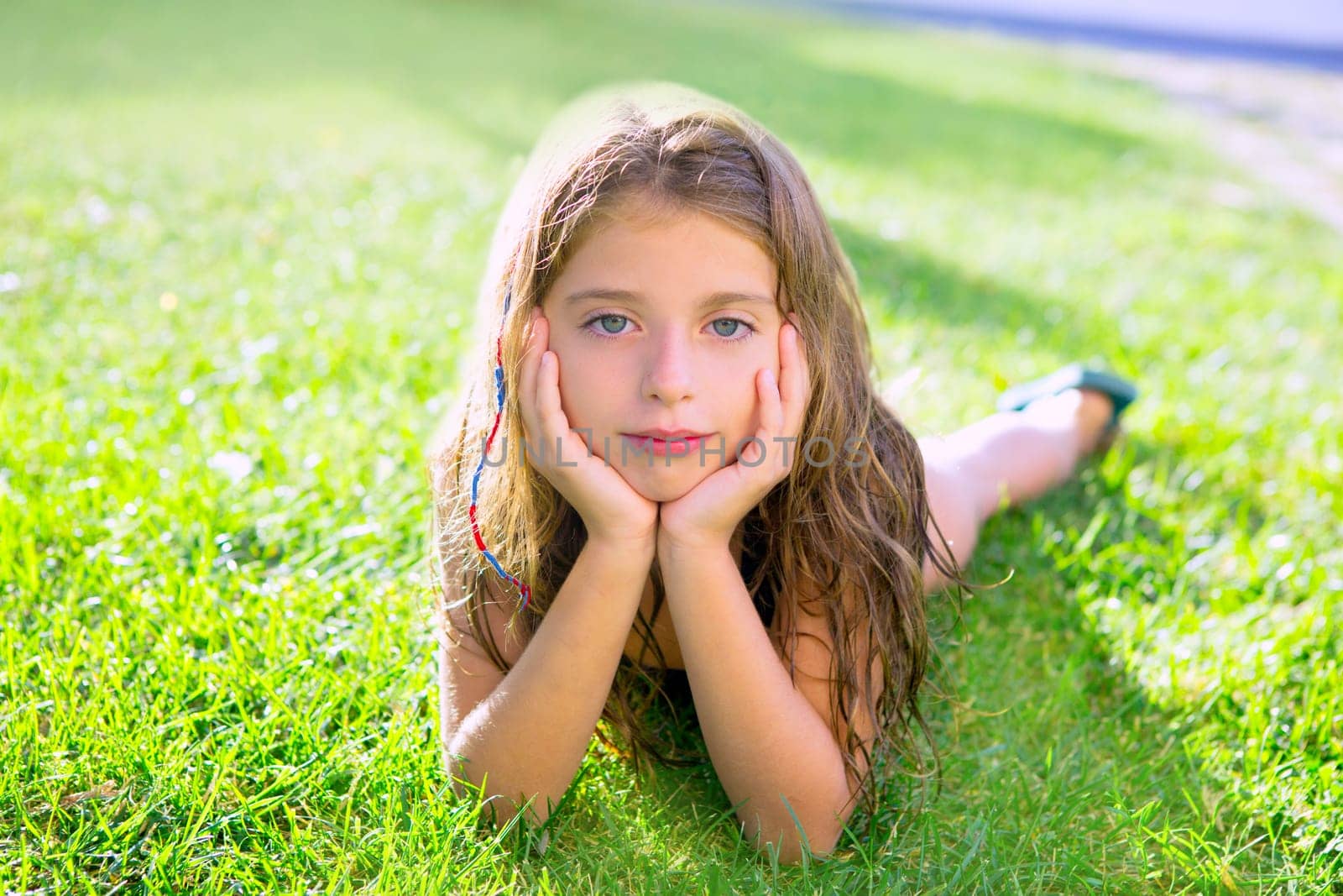 blue eyes children girl relaxed on the garden grass lying with hands in face