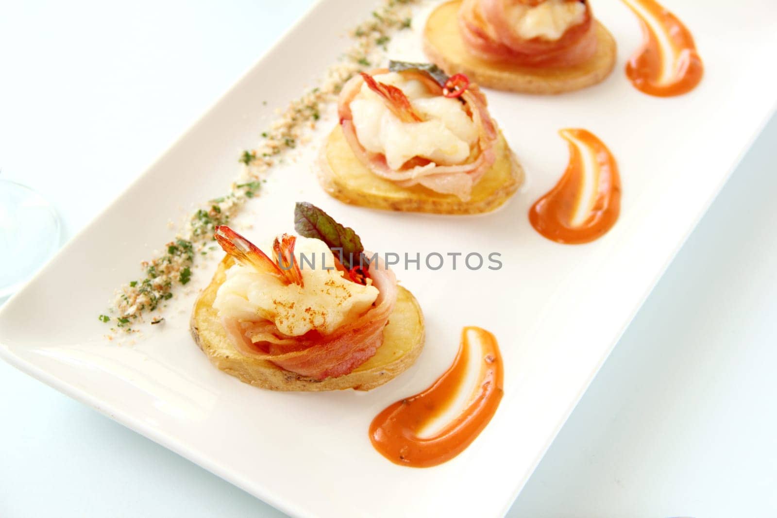 Delicious and delicate shrimps wrapped in bacon on potato slices with a spinach leaf.