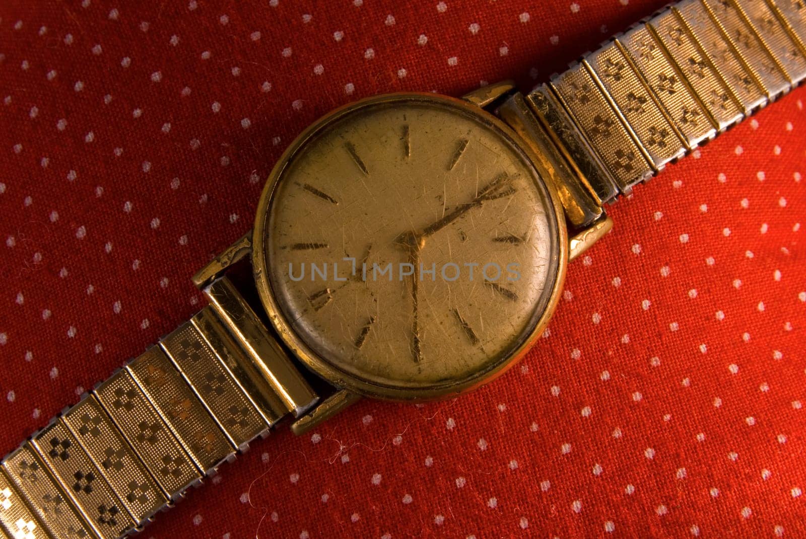 Retro golden wristwatch close up on red vintage cloth background.