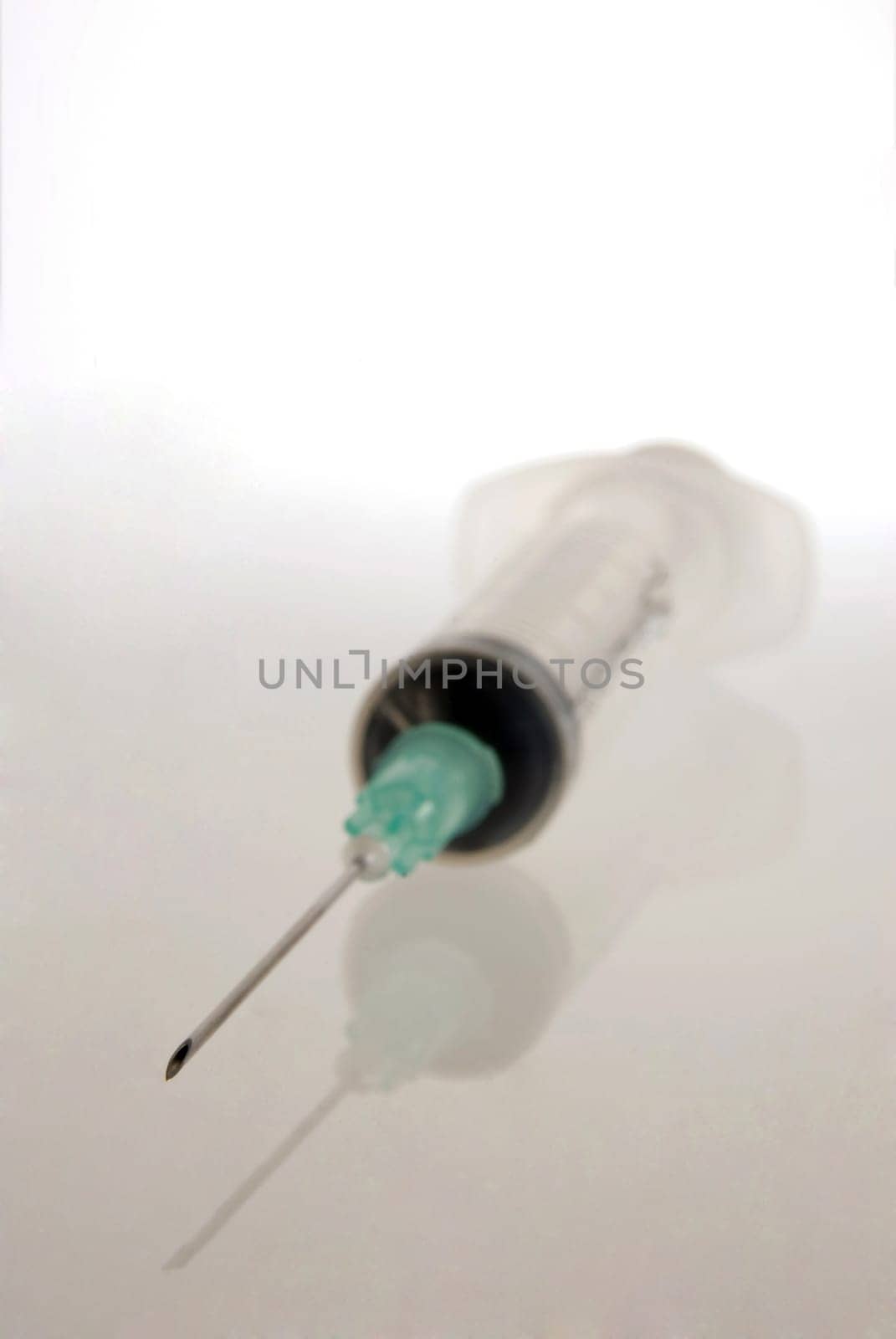 Srynge close up with focus in its needle and object reflection on clear gray background.