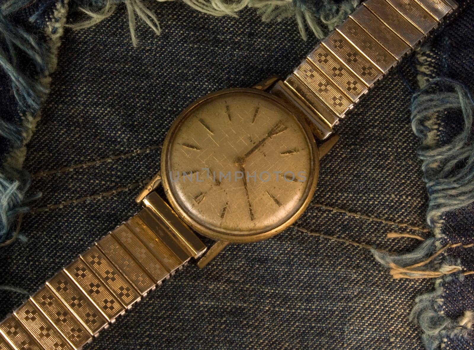 Retro golden wristwatch close up over blue jean cloth background.