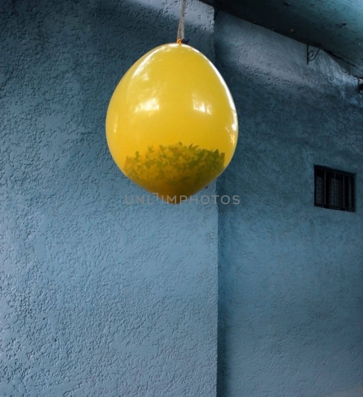Pinata. Hanging yellow balloon with gifts and confetti inside. Rough wall texture background