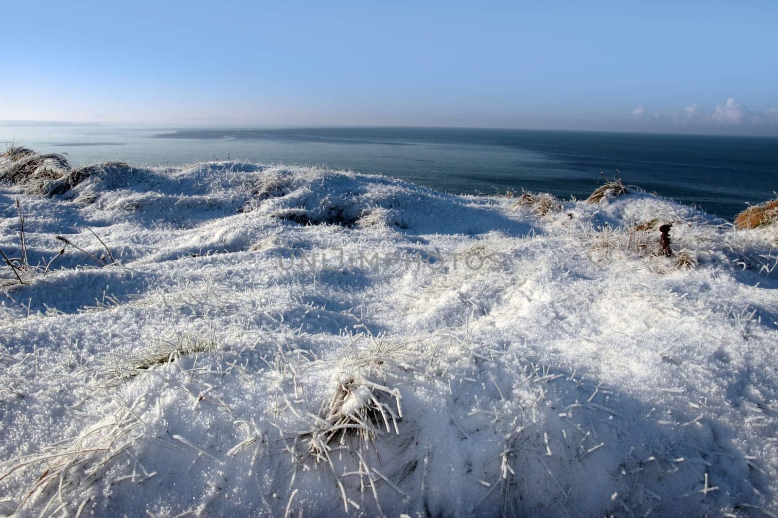 a seasonal snow frosty covered grass ditch with a view of the atlantic ocean and a  blue cloudy sky background