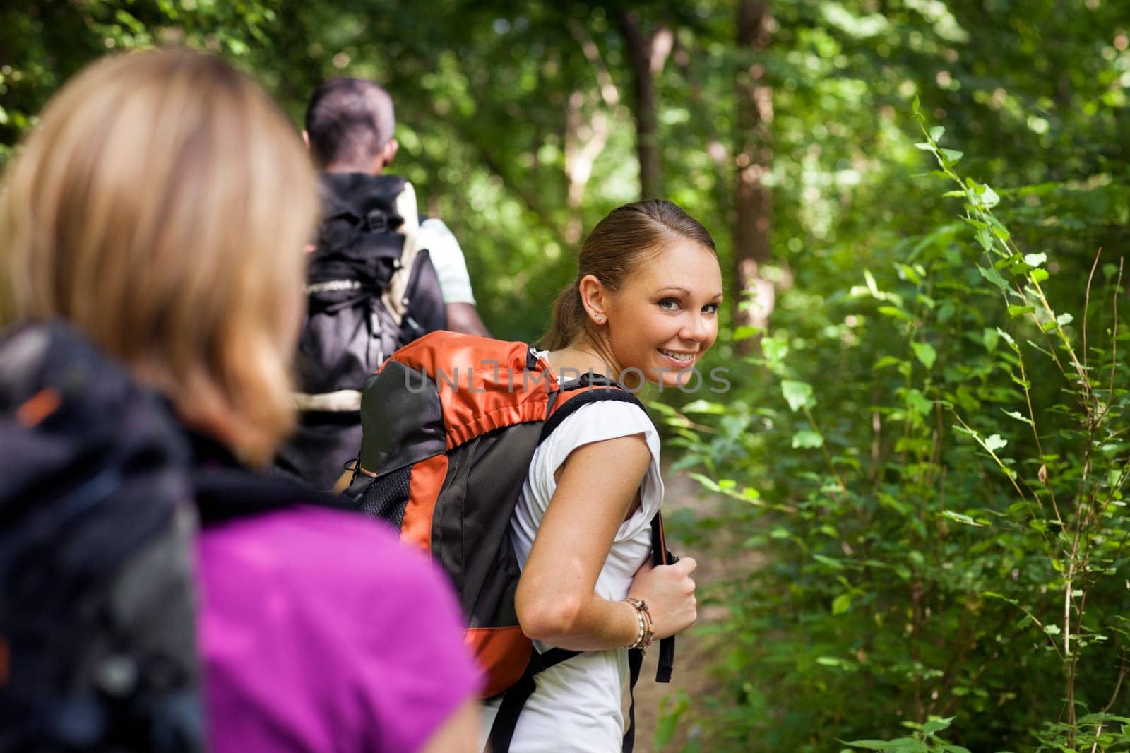 group of man and women during hiking excursion in woods, with woman looking at camera over shoulders and smiling. Waist up