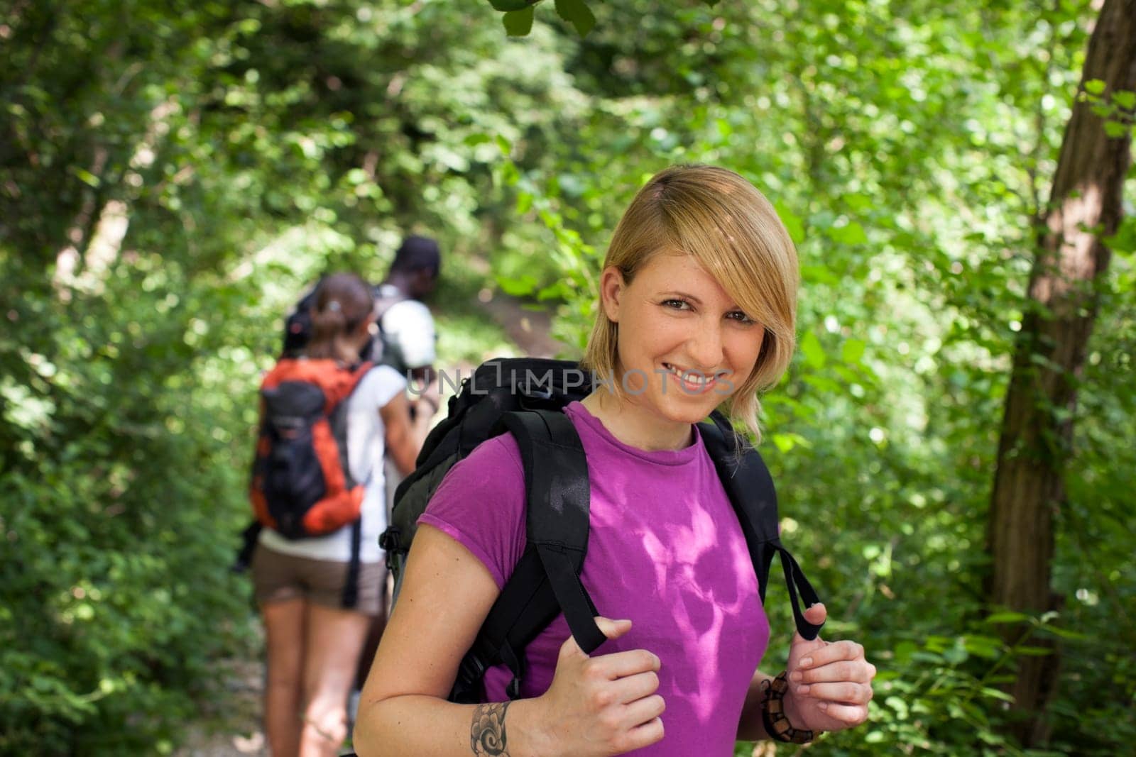 group of man and women during hiking excursion in woods, with woman looking at camera and smiling. Waist up