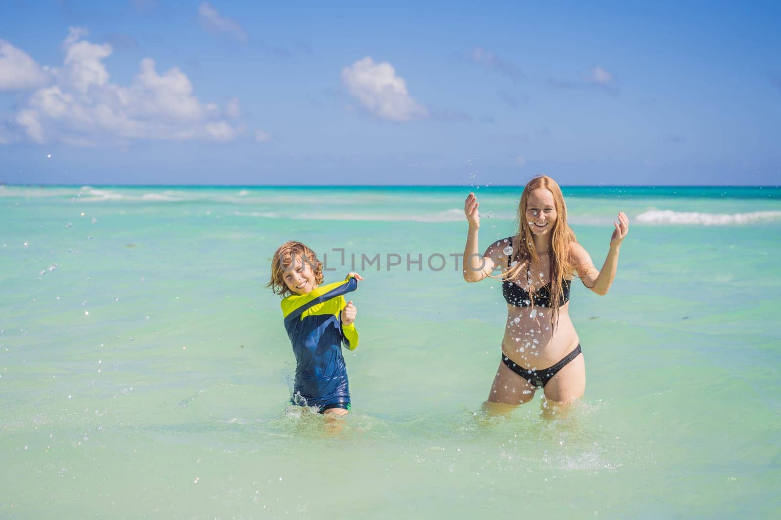 A radiant pregnant mother and her excited son share a tender moment on a serene, snow-white beach, celebrating family love amidst nature's beauty by galitskaya