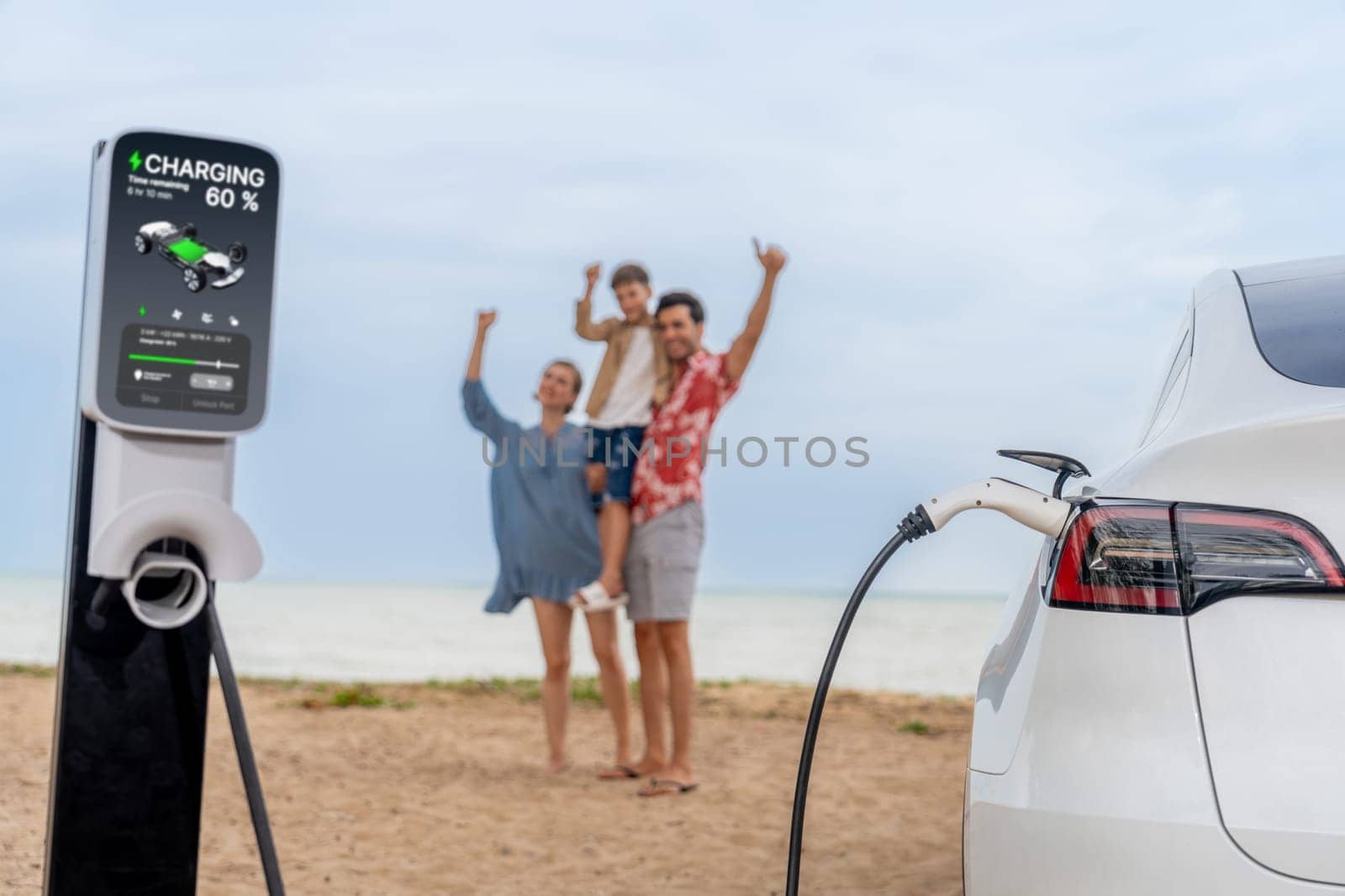 Alternative family vacation trip traveling by the beach with electric car recharging battery from EV charging station with blurred cheerful and happy family enjoying the seascape background. Perpetual