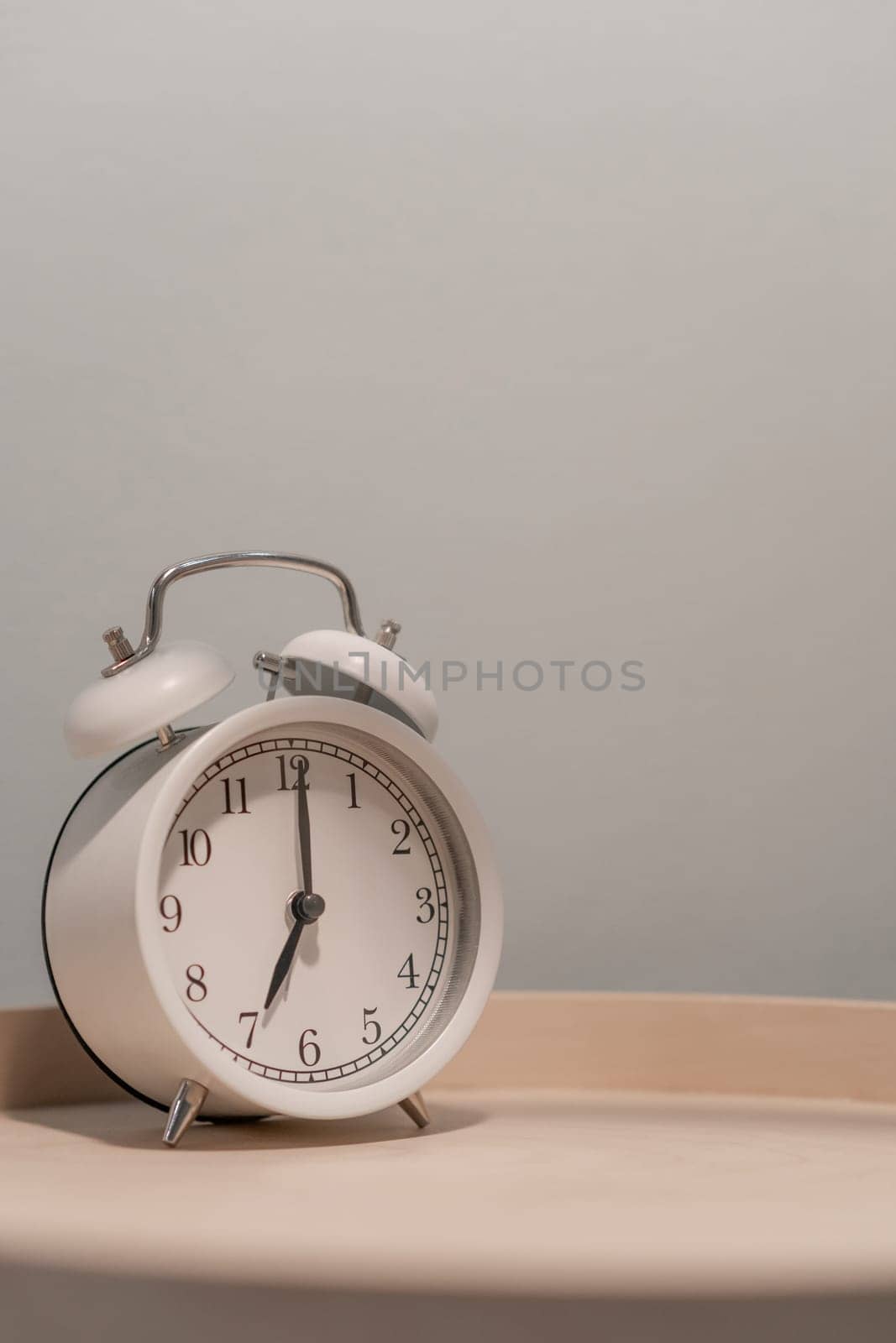 Close-up of a round white alarm clock on a table in the bedroom. by AnatoliiFoto