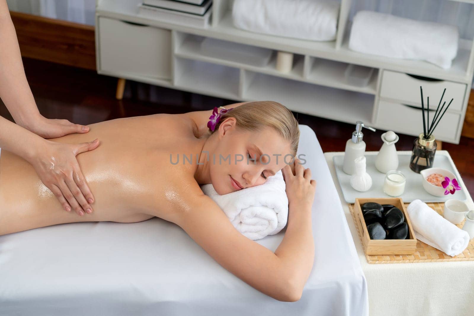 Caucasian woman customer enjoying relaxing anti-stress spa massage and pampering with beauty skin recreation leisure in day light ambient salon spa at luxury resort or hotel. Quiescent