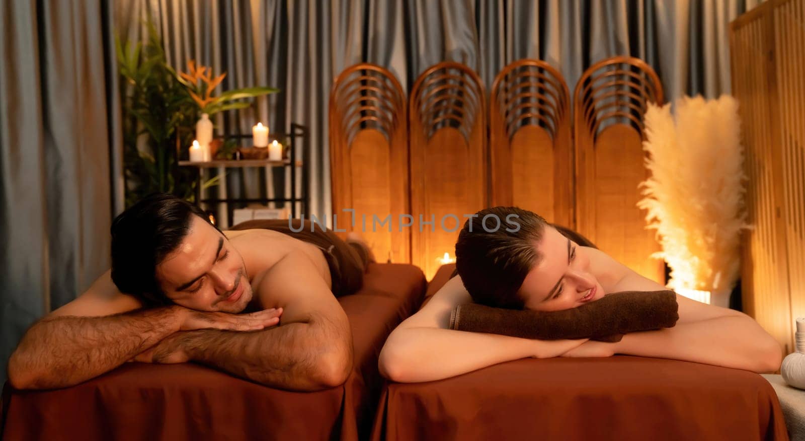 Caucasian couple customer enjoying relaxing anti-stress spa massage and pampering with beauty skin recreation leisure in warm candle lighting ambient salon spa at luxury resort or hotel. Quiescent