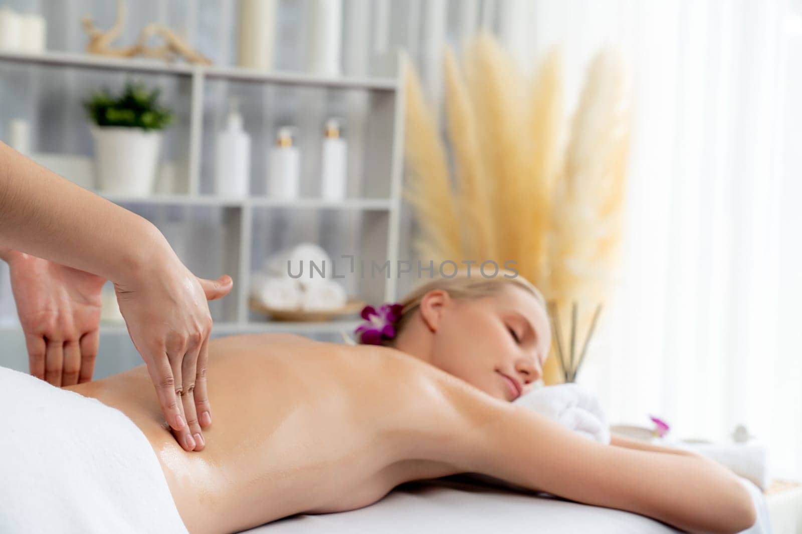 Caucasian woman customer enjoying relaxing anti-stress spa massage and pampering with beauty skin recreation leisure in day light ambient salon spa at luxury resort or hotel. Quiescent