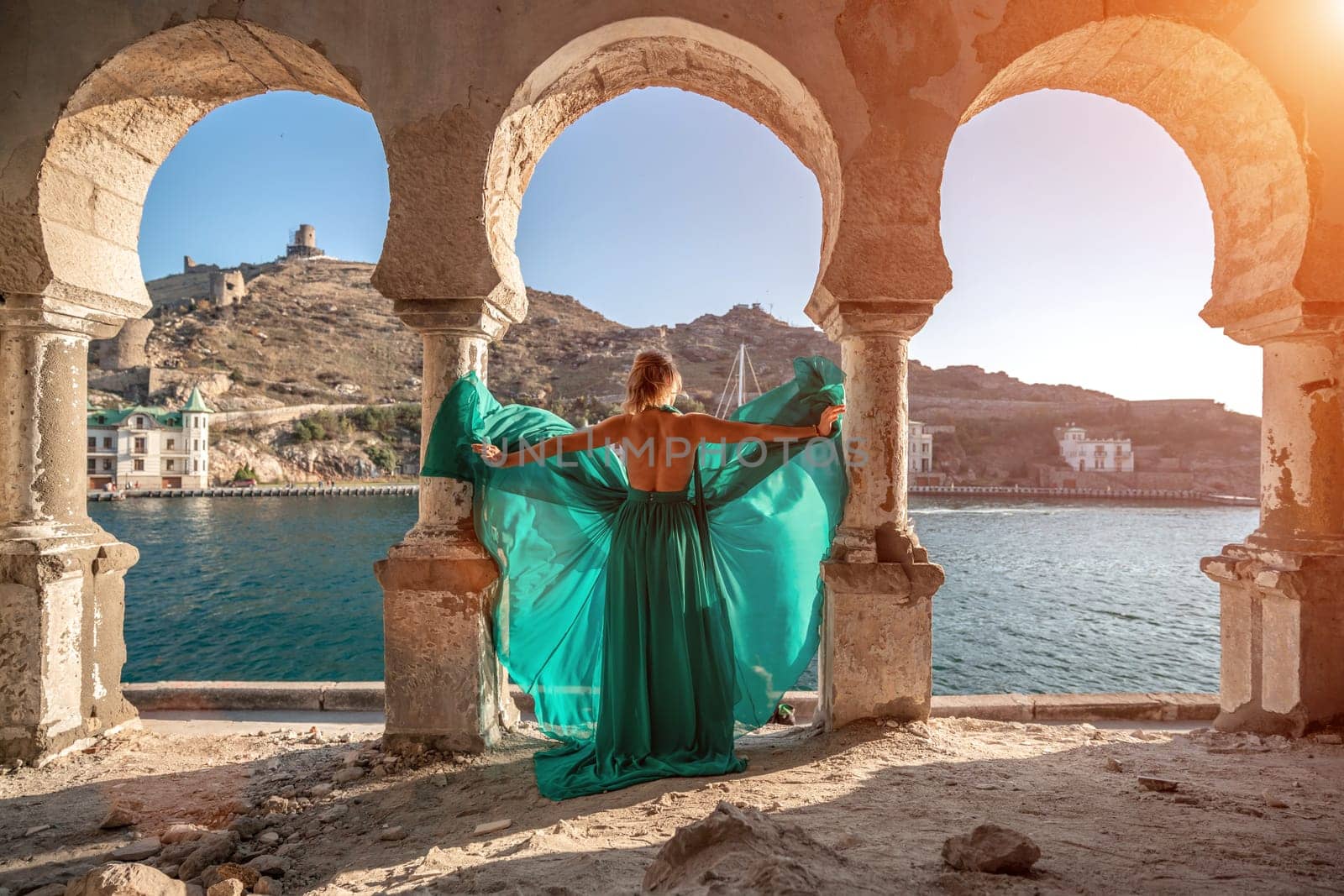 Woman dress sea columns. Rear view of a happy blonde woman in a long mint dress posing against the backdrop of the sea in an old building with columns