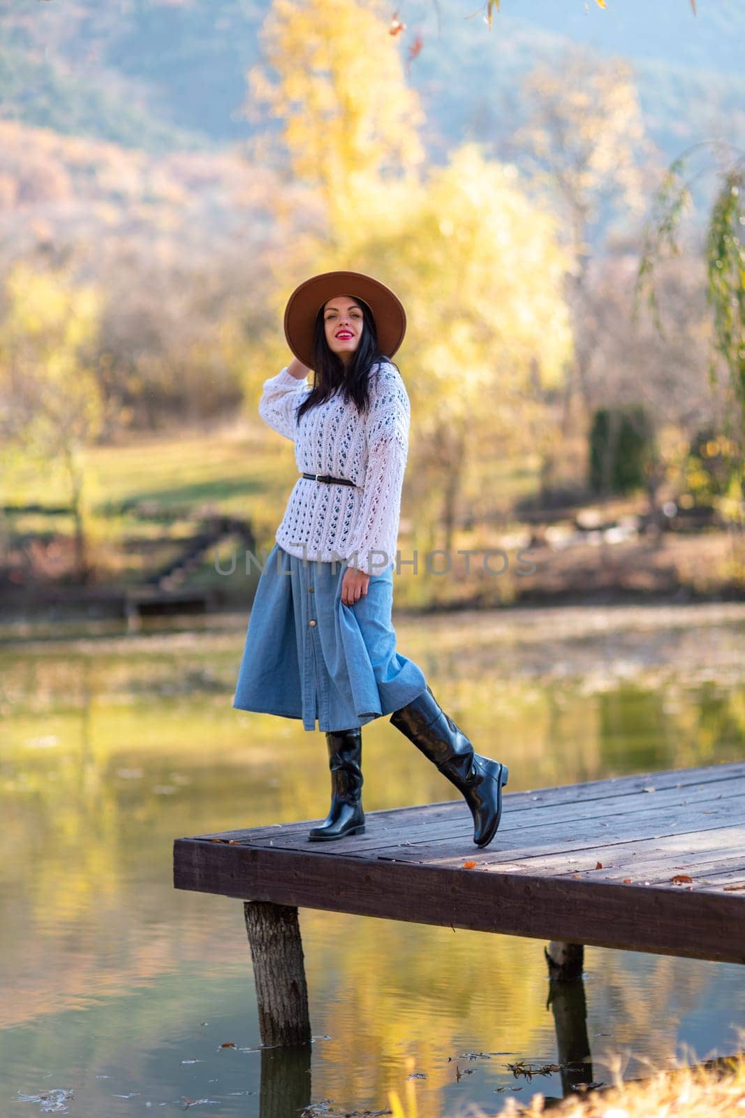 Autumn lake woman. She stands by a pond on a wooden pier in autumn and admires nature. The concept of tourism, weekends outside the city