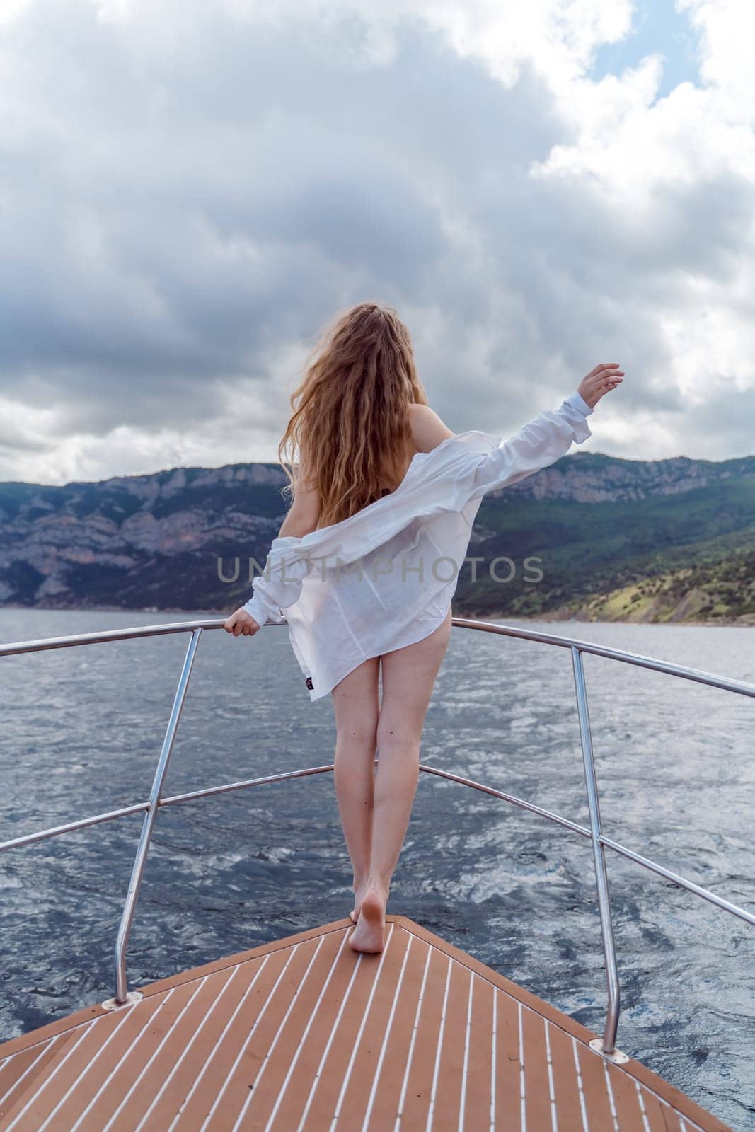 Woman on a yacht. Happy model in a swimsuit posing on a yacht against a blue sky with clouds and mountains by Matiunina
